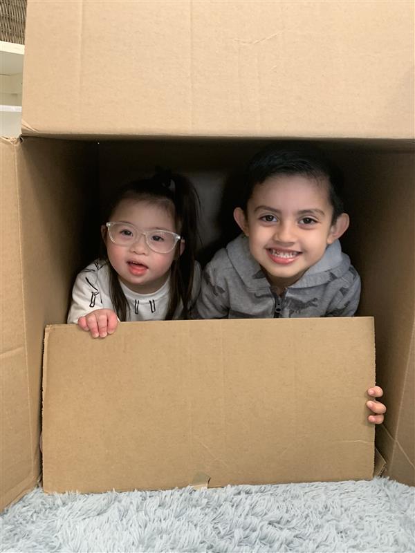 Two kids peeking through a cardboard box